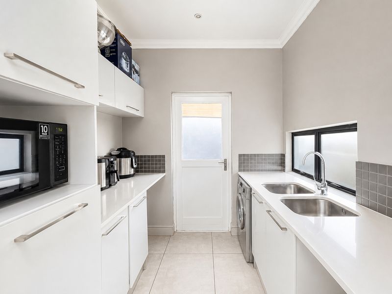 A clean and functional scullery featuring modern white cabinetry, stone countertops, a double sink, and direct access to the exterior.