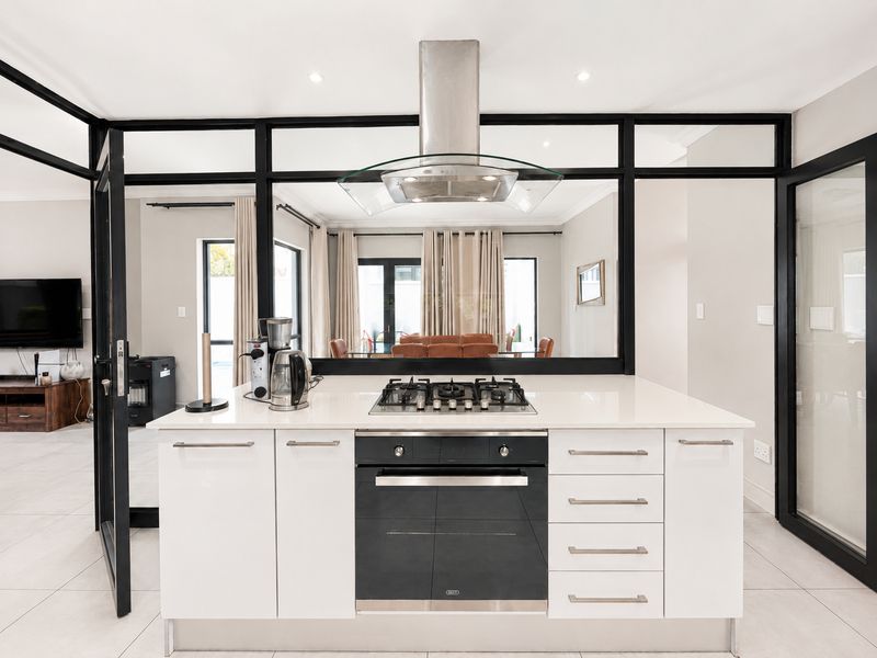 Modern kitchen island featuring a gas hob, built-in oven, and extractor fan, set against a stylish black-framed glass partition.