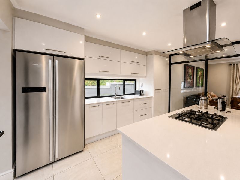 Modern kitchen featuring high-gloss white cabinetry, stone countertops, a central island with a gas hob, and a sleek stainless steel extractor fan.