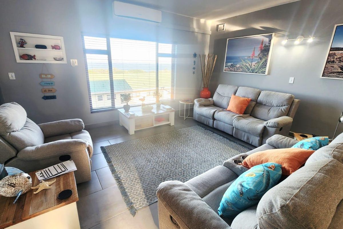 A comfortable living room featuring tiled flooring, a wall-mounted split-system air conditioner, and large windows with venetian blinds offering natural light.
