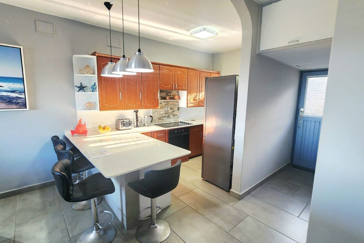 A functional kitchen featuring wooden cabinetry, stone countertops, a breakfast bar, and tiled flooring, seamlessly connected to the living area via an archway.