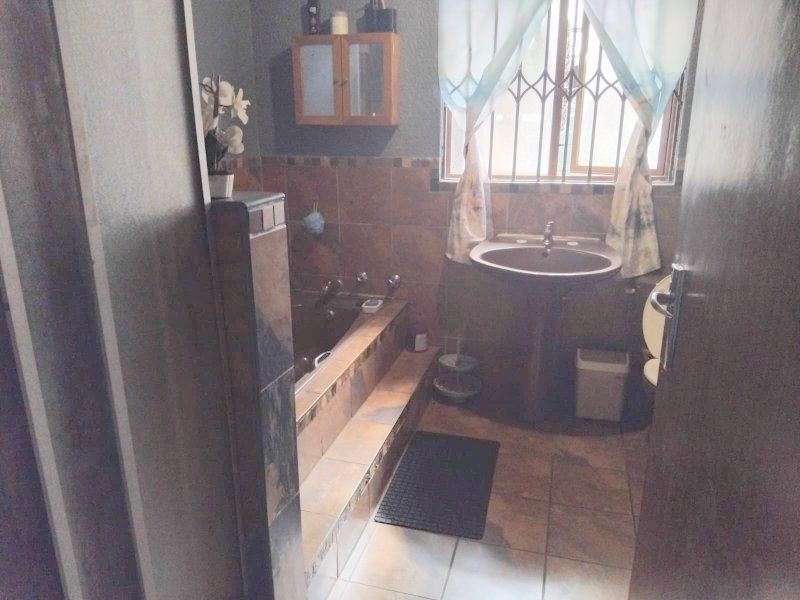 A functional bathroom featuring a built-in tiled bathtub, pedestal basin, and wall-mounted storage cabinet with dated tile finishes.
