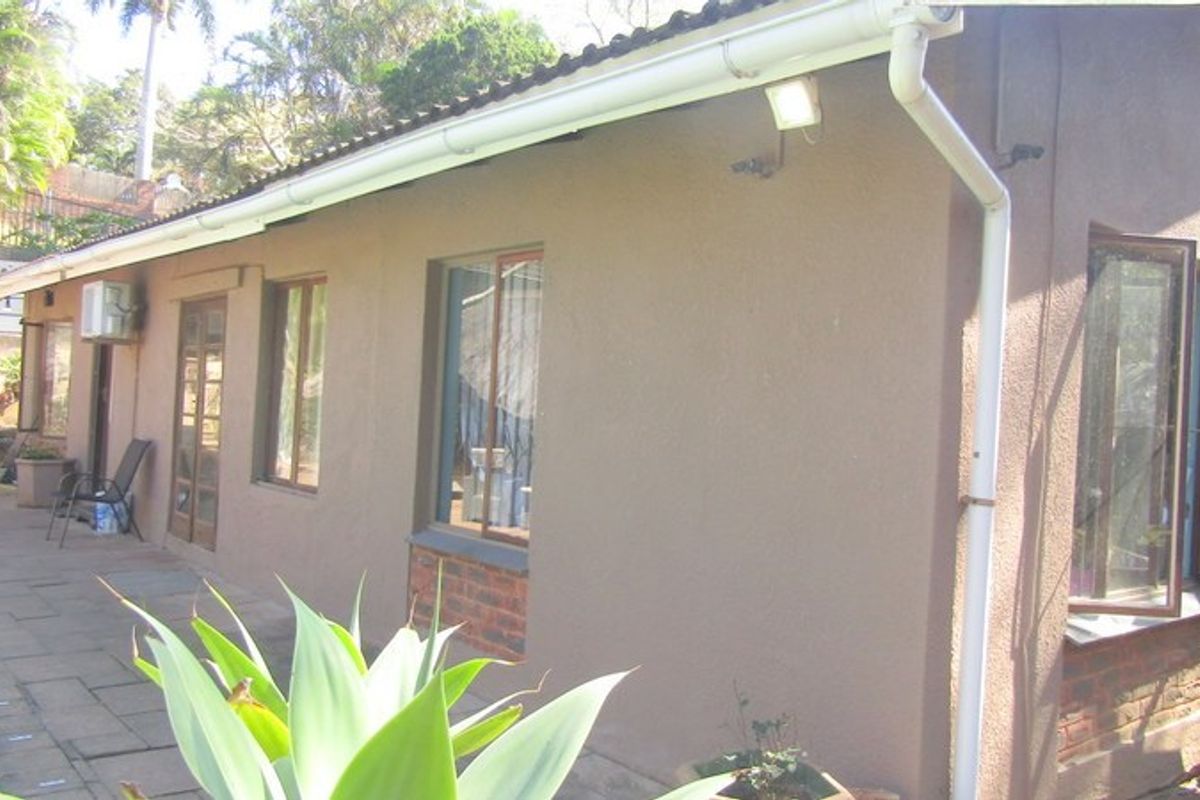 Rear exterior view of the house featuring a paved patio area, guttering, and security lighting along the side wall.