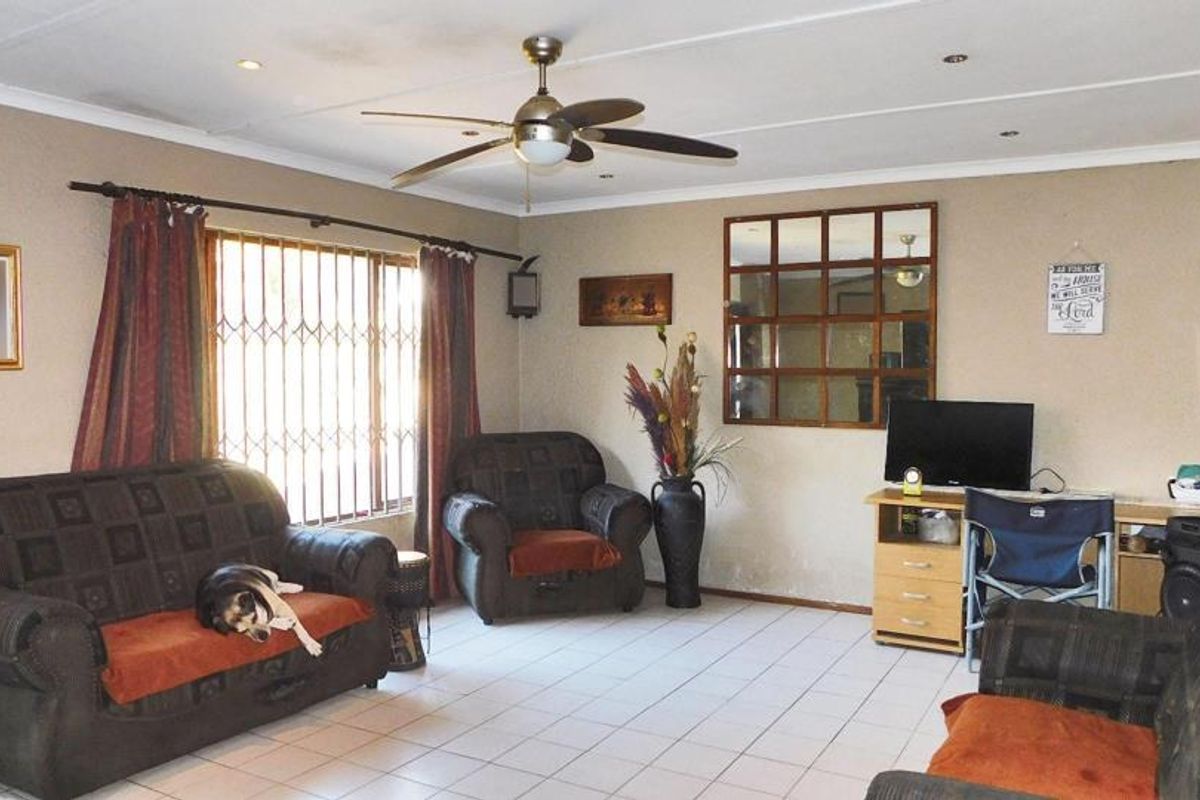 A spacious living room featuring tiled flooring, a ceiling fan, recessed lighting, and a security gate over the window.