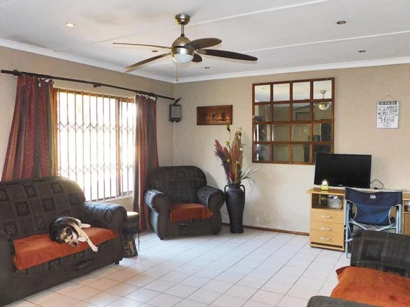 A spacious living room featuring tiled flooring, a ceiling fan, recessed lighting, and a security gate over the window.