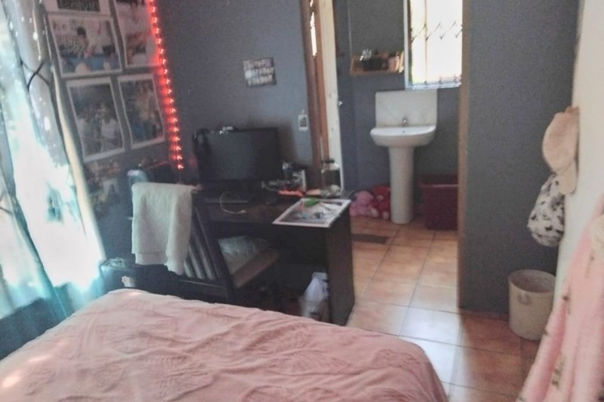 A bedroom featuring tiled flooring and an en-suite area with a pedestal basin and security bars on the window.