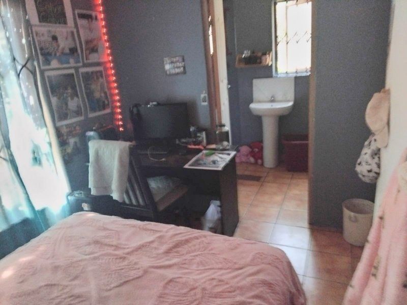 A bedroom featuring tiled flooring and an en-suite area with a pedestal basin and security bars on the window.