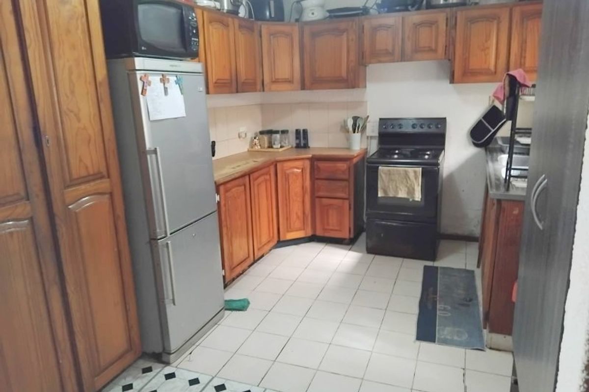 A functional kitchen featuring traditional wooden cabinetry, tiled flooring, and a freestanding stove, offering potential for a modern cosmetic update.