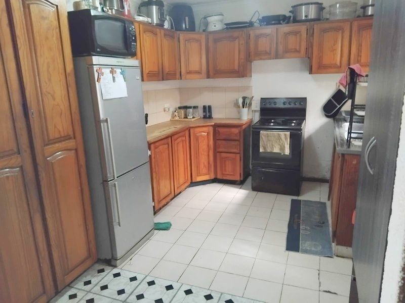 A functional kitchen featuring traditional wooden cabinetry, tiled flooring, and a freestanding stove, offering potential for a modern cosmetic update.