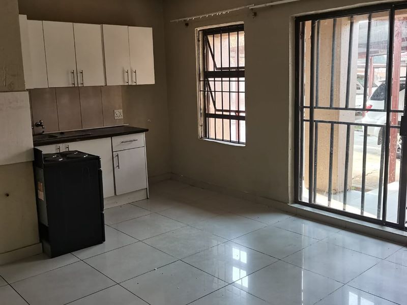 Open plan kitchen and living area featuring tiled flooring, basic cabinetry, and sliding door access to the exterior with security bars.