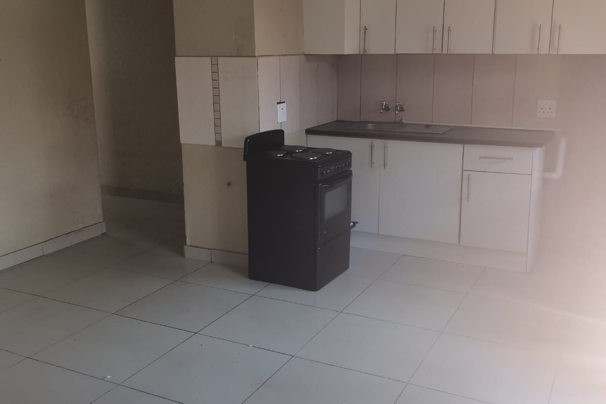 A compact, empty kitchen featuring white cabinetry, a stainless steel sink, tiled flooring, and a freestanding stove, ready for renovation or modernization.