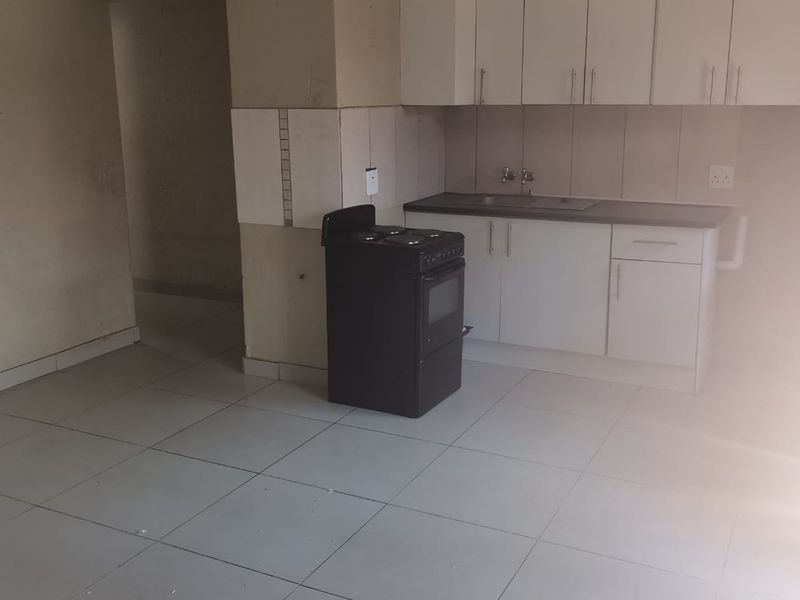A compact, empty kitchen featuring white cabinetry, a stainless steel sink, tiled flooring, and a freestanding stove, ready for renovation or modernization.