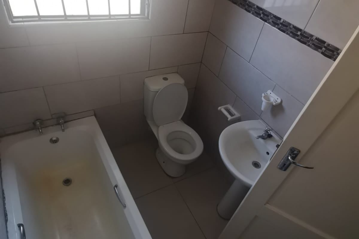 A compact bathroom featuring a bathtub, pedestal basin, and toilet with tiled finishes and security bars on the window.