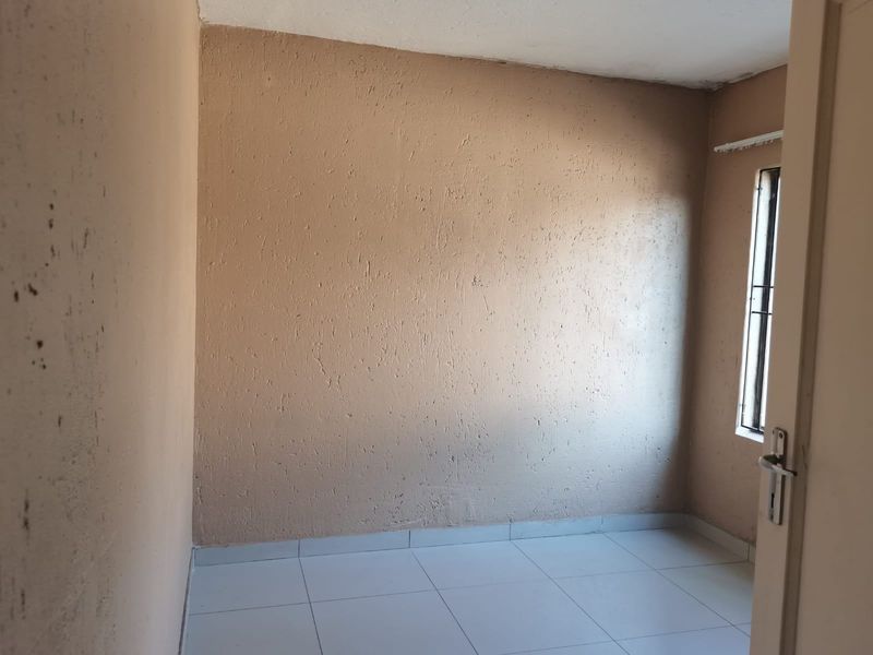 An empty bedroom featuring tiled flooring, textured walls, and a window with security bars, requiring cosmetic updates to improve its overall condition.