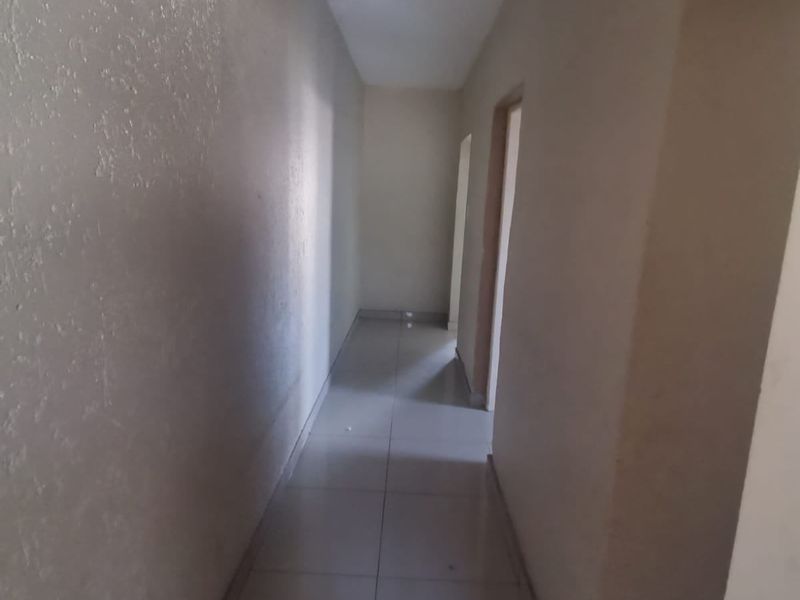 A simple, empty residential hallway featuring neutral textured walls and light-colored floor tiles, providing access to adjacent rooms.