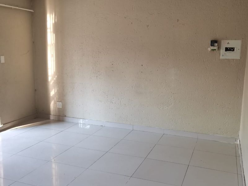 An empty living area featuring white ceramic floor tiles, textured walls, and a wall-mounted electrical distribution board.