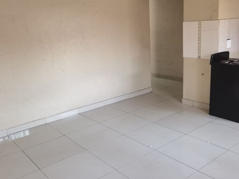 An empty open-plan living area featuring white ceramic floor tiles and neutral wall finishes, providing a blank canvas for potential interior design updates.