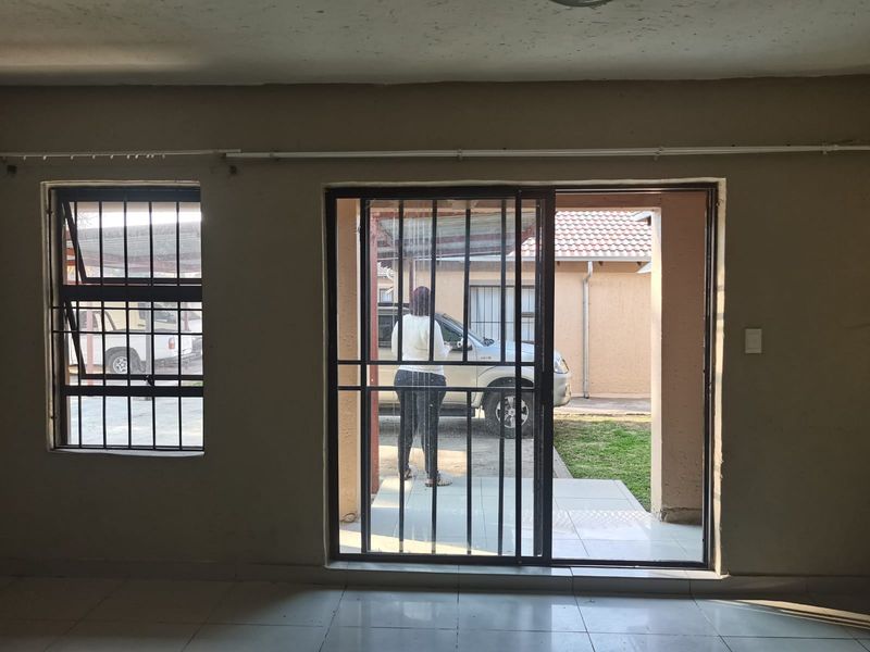 An empty living area featuring tiled flooring, security bars on windows and sliding doors, with direct access to the exterior.