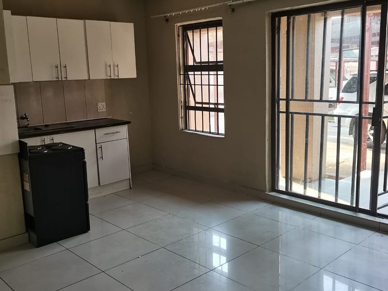 An open-plan kitchen and living area featuring tiled floors, basic cabinetry, and security bars on the windows and sliding door.