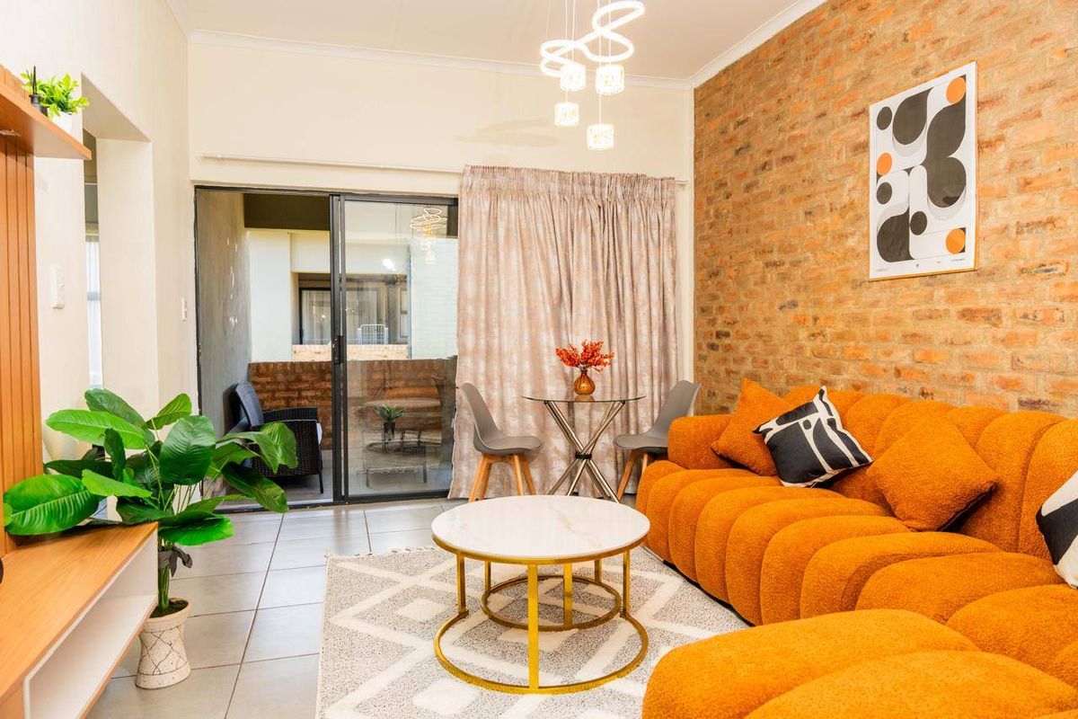 A bright living room featuring an exposed brick accent wall, tiled flooring, and a sliding glass door providing access to an outdoor patio area.