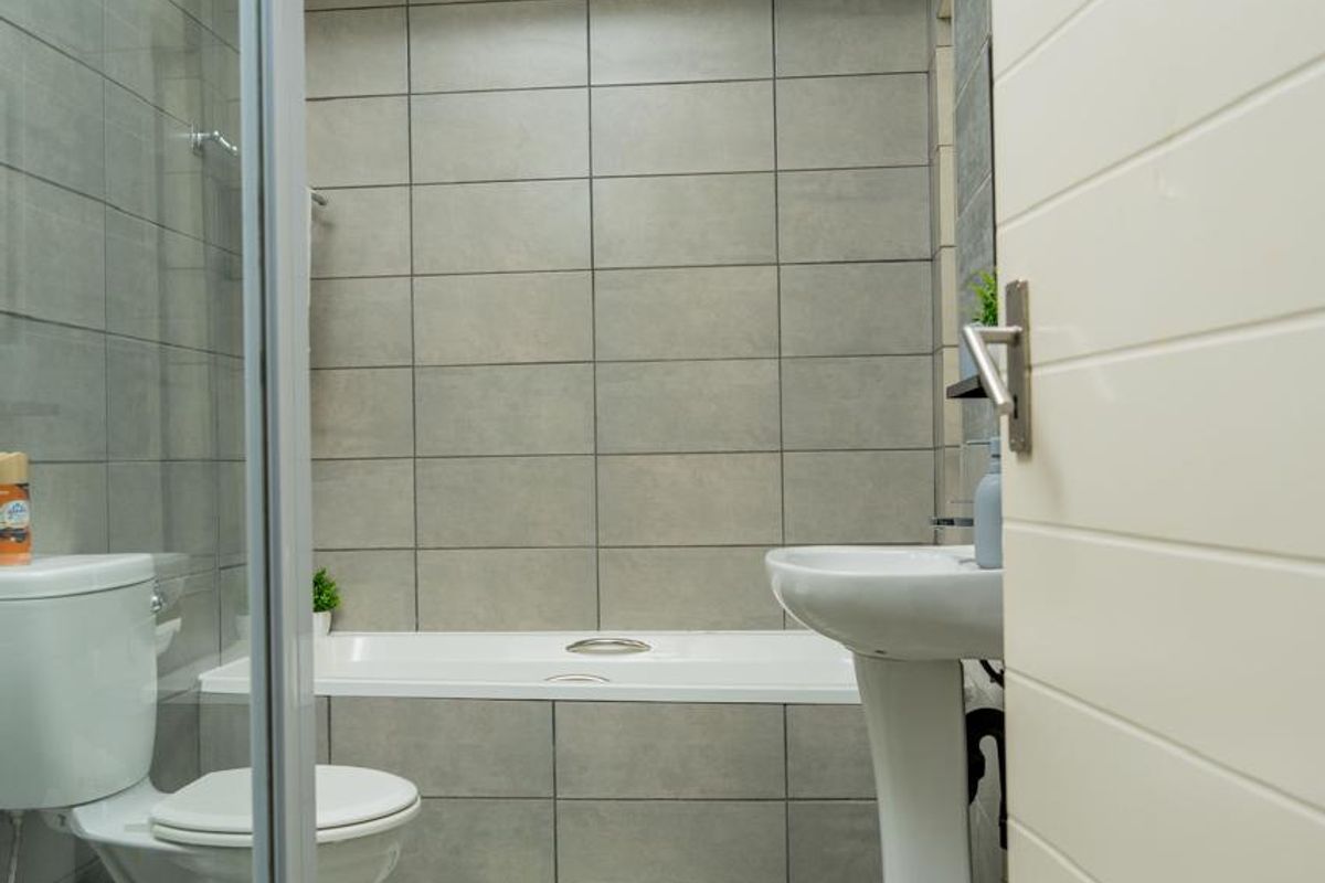 A clean, modern bathroom featuring a pedestal basin, built-in bathtub, and a separate glass-enclosed shower with neutral grey wall and floor tiling.