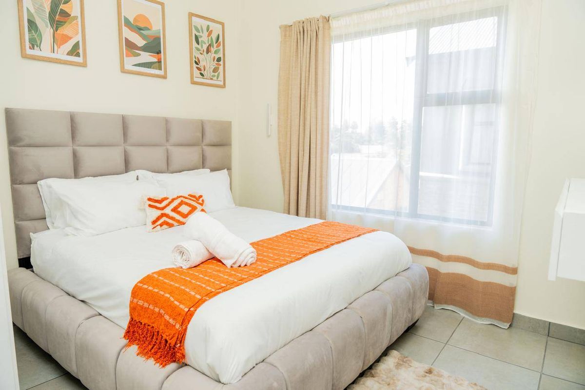 A well-lit bedroom featuring neutral wall tones, tiled flooring, and a large window with installed curtain tracks.