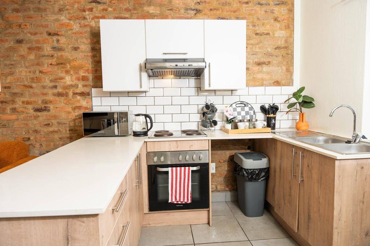 A modern kitchen featuring exposed brick walls, subway tile backsplash, stone countertops, and integrated appliances including an oven and extractor fan.