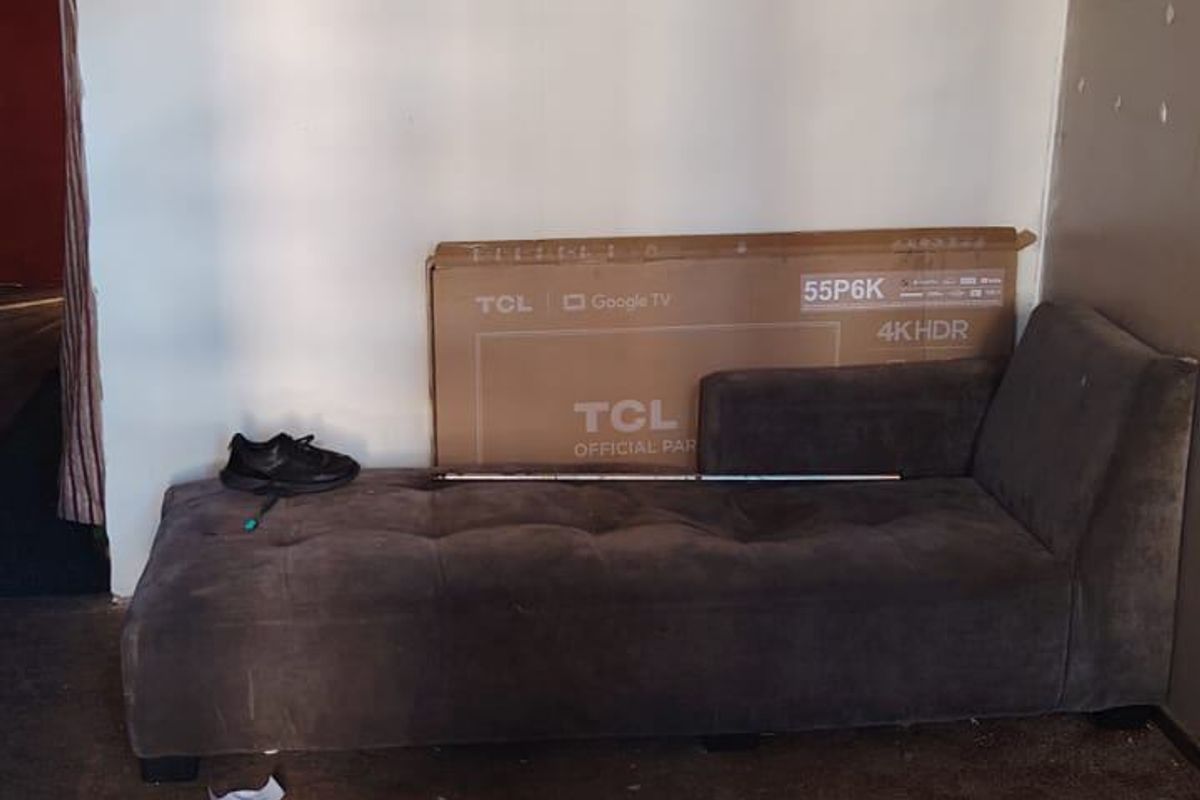 A living area featuring tiled flooring transitioning to carpet, with visible wear and tear on the wall surfaces and floor finishes.