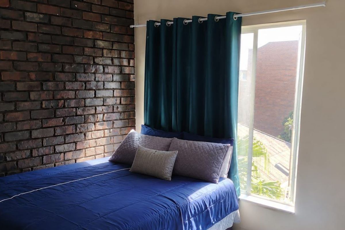 A bedroom featuring a distinctive exposed brick feature wall and a large window that provides natural light.