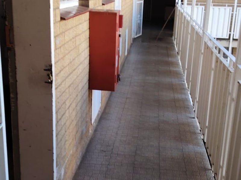 An exterior apartment access walkway featuring brick walls, metal balustrades, and fire safety equipment.