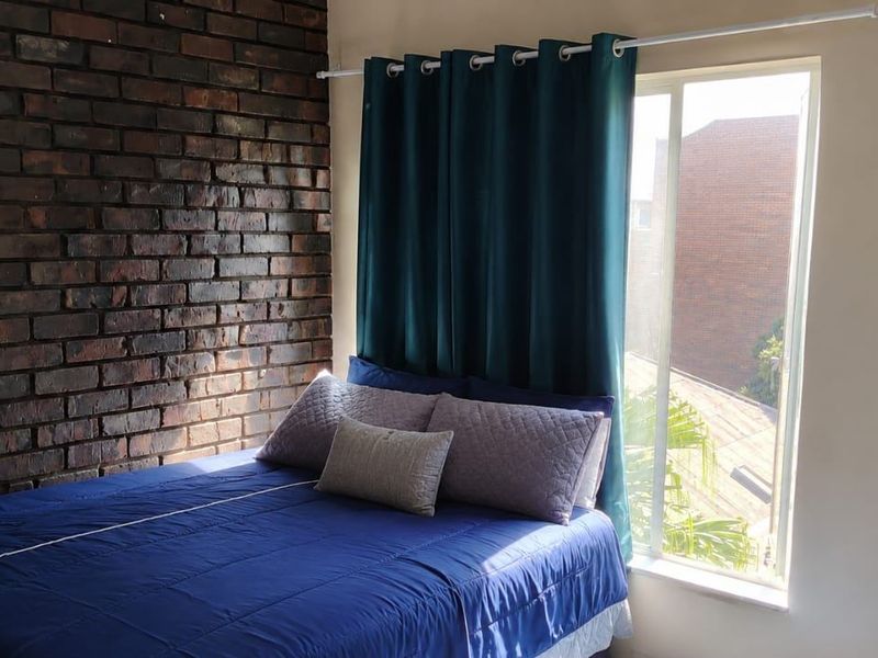 A bedroom featuring an exposed brick feature wall and a large sliding window providing natural light.
