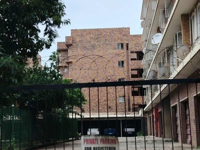 Exterior view of an apartment complex featuring a secure gated entrance, brick facade, and covered parking area.