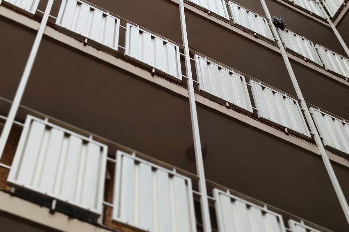Low angle view of an apartment building facade featuring multiple levels of balconies with white metal railings.