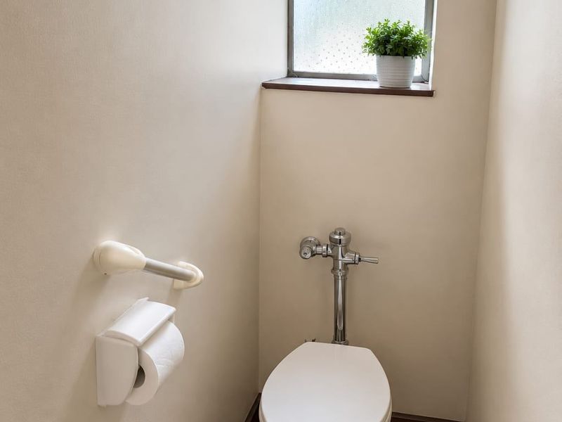 A compact bathroom featuring a standard flush valve toilet, tiled flooring, and a small obscured glass window for natural light.