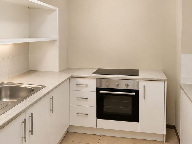 A functional kitchen featuring white cabinetry, laminate countertops, a stainless steel sink, and integrated oven with electric cooktop.