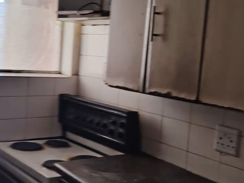 A dated kitchen featuring built-in cabinetry, a tiled backsplash, and a freestanding stove, requiring significant renovation and cosmetic updates.