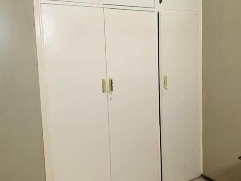 A bedroom featuring built-in white cupboards with overhead storage and tiled flooring, presenting a dated aesthetic in need of cosmetic updates.