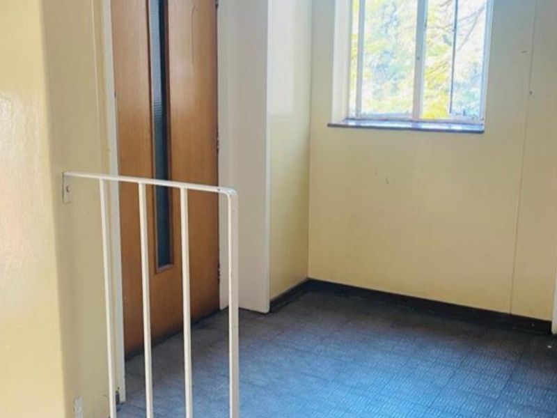 A functional apartment hallway featuring tiled flooring, a metal safety balustrade, and access to a staircase and doorway.