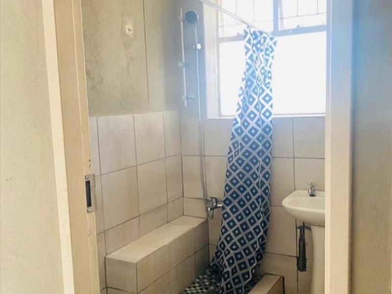 A dated bathroom featuring a pedestal sink, a tiled shower area with a built-in bench, and a window for natural light.