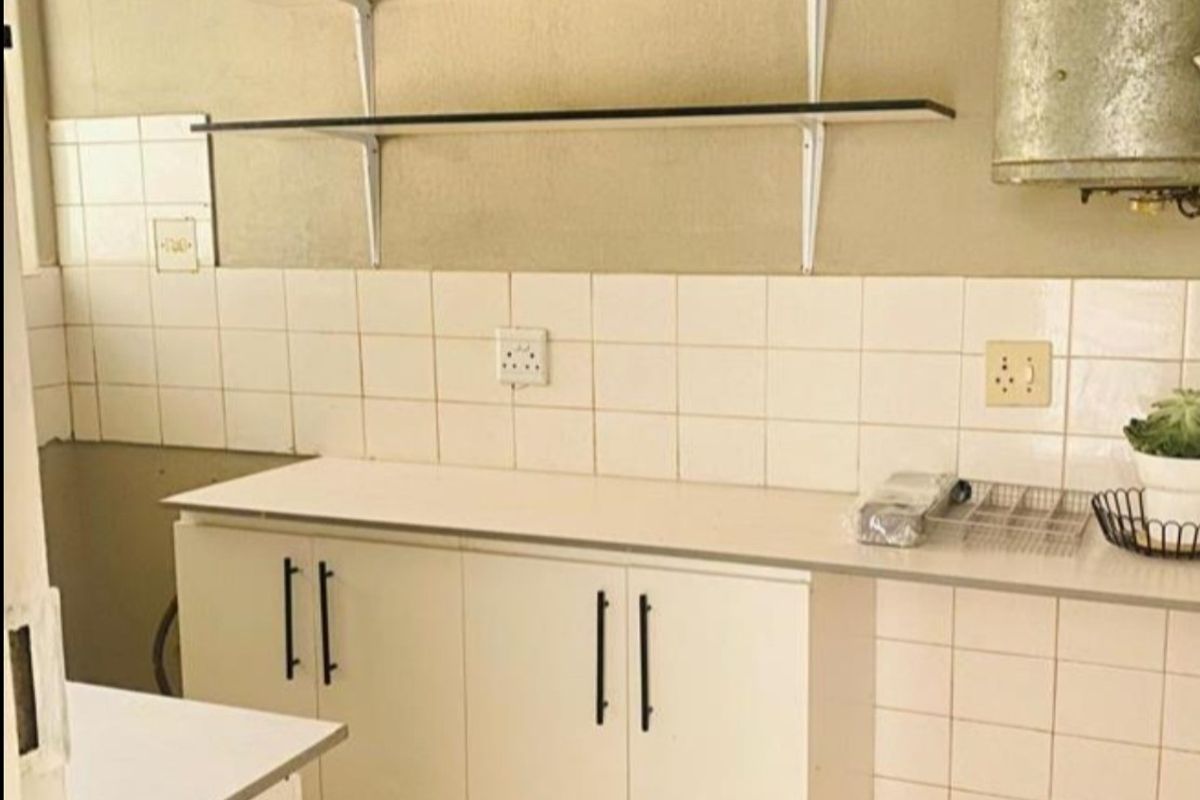A functional kitchen space featuring built-in cabinetry, tiled backsplash, and wall-mounted shelving, offering a blank canvas for potential modern renovation.