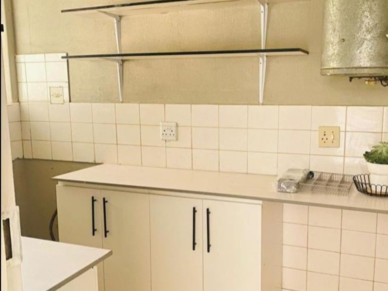 A functional kitchen space featuring built-in cabinetry, tiled backsplash, and wall-mounted shelving, offering a blank canvas for potential modern renovation.