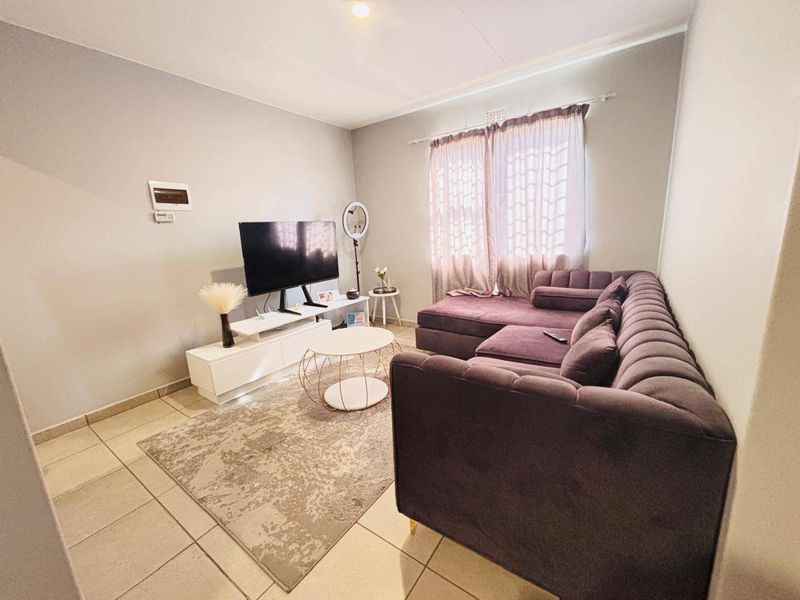 A comfortable living room featuring neutral tiled flooring and natural light through window curtains, providing a functional and inviting space.