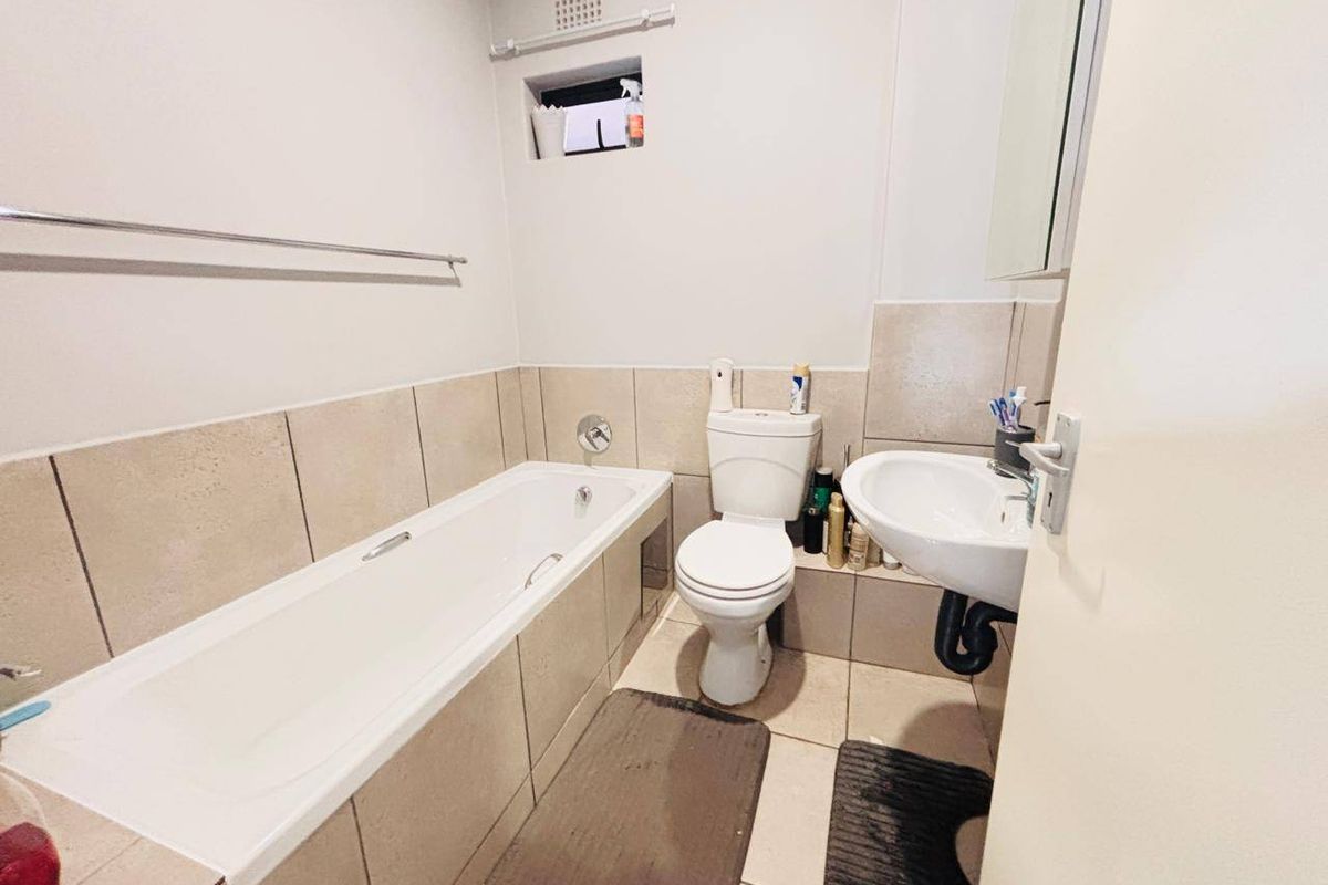 A functional bathroom featuring a bathtub, pedestal basin, and toilet with neutral wall tiling and a small ventilation window.