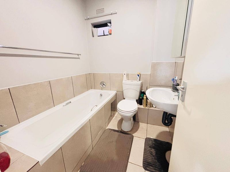 A functional bathroom featuring a bathtub, pedestal basin, and toilet with neutral wall tiling and a small ventilation window.