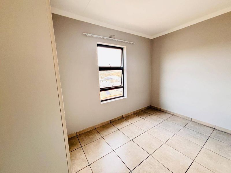 A clean, empty bedroom featuring neutral wall paint, tiled flooring, and a built-in cupboard, offering a blank canvas for personalization.