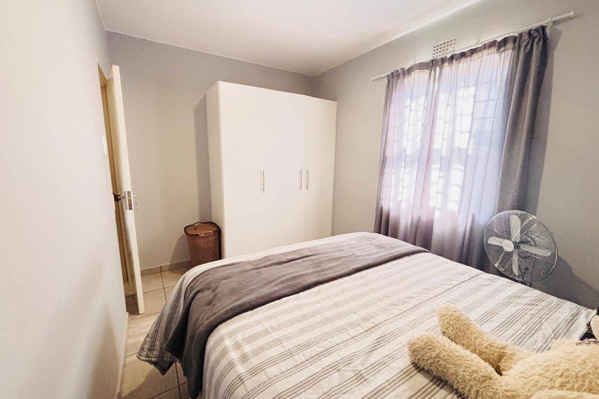 A functional bedroom featuring tiled flooring, a built-in wardrobe, and a window fitted with security bars.