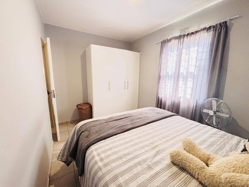 A functional bedroom featuring tiled flooring, a built-in wardrobe, and a window fitted with security bars.
