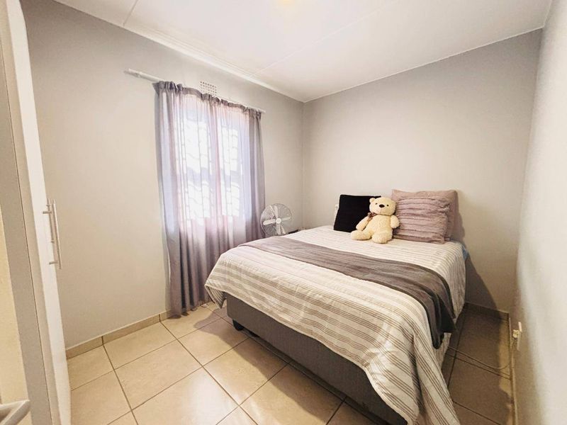 A compact bedroom featuring neutral wall tones, tiled flooring, and a built-in wardrobe, offering a clean and functional living space.