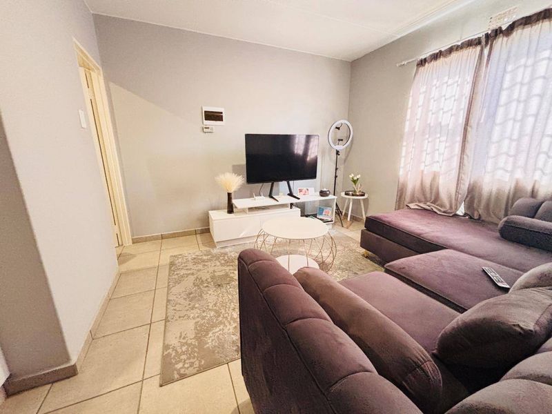 A living room featuring neutral wall paint and tiled flooring, with natural light provided by a window with curtain rails.