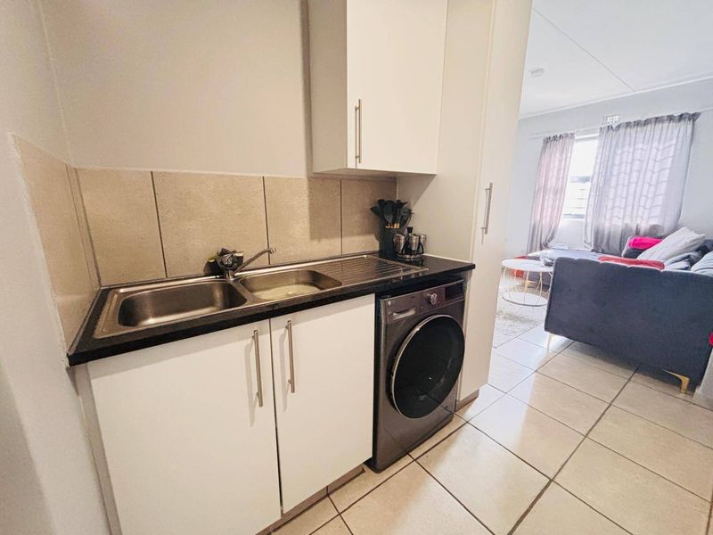 Compact kitchen area featuring white cabinetry, a stainless steel double sink, tiled backsplash, and dedicated space for a washing machine.